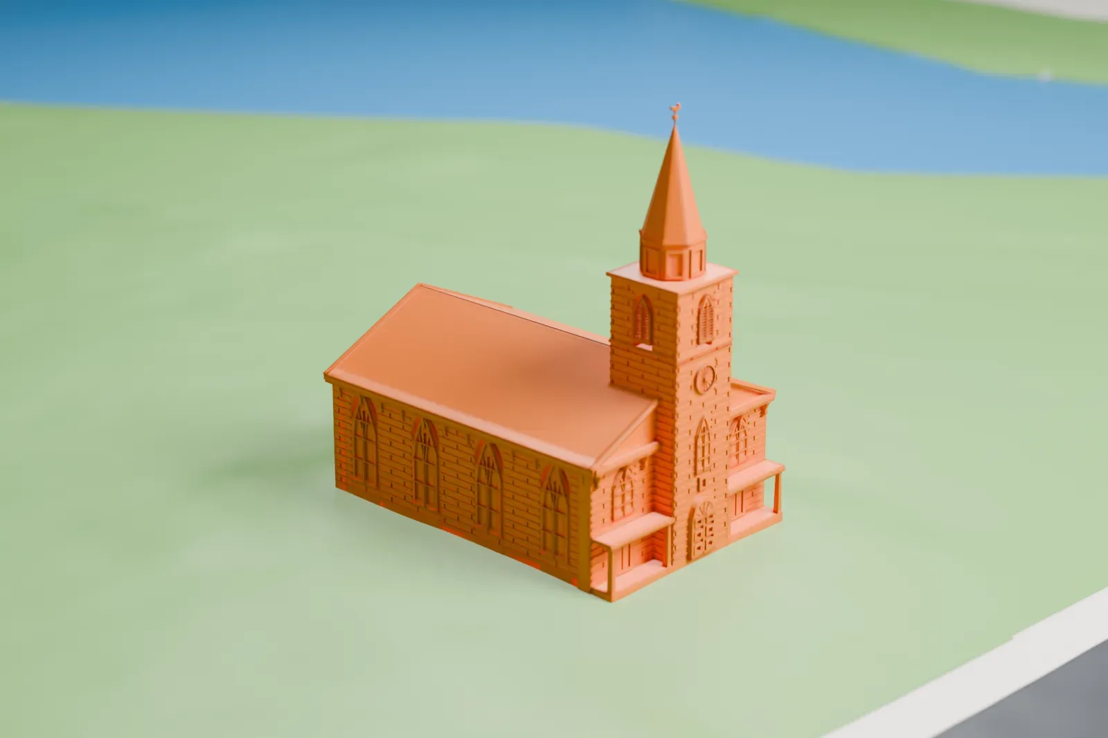 A white 3D print of South Schraalenburgh Church, a long church with a tower and tall spire at one end, standing on open grass beside a road.