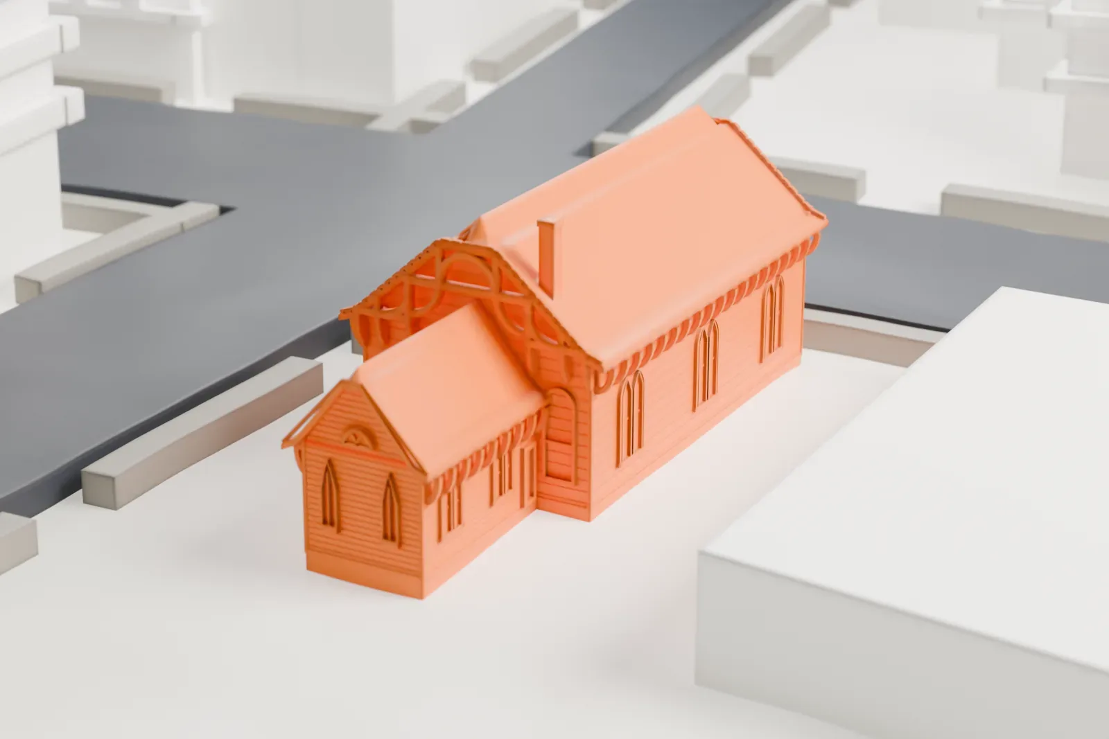 A white 3D print of St. James Church, a small gabled church with a lower rear wing and pointed-arch windows, on a corner lot beside streets and larger buildings.