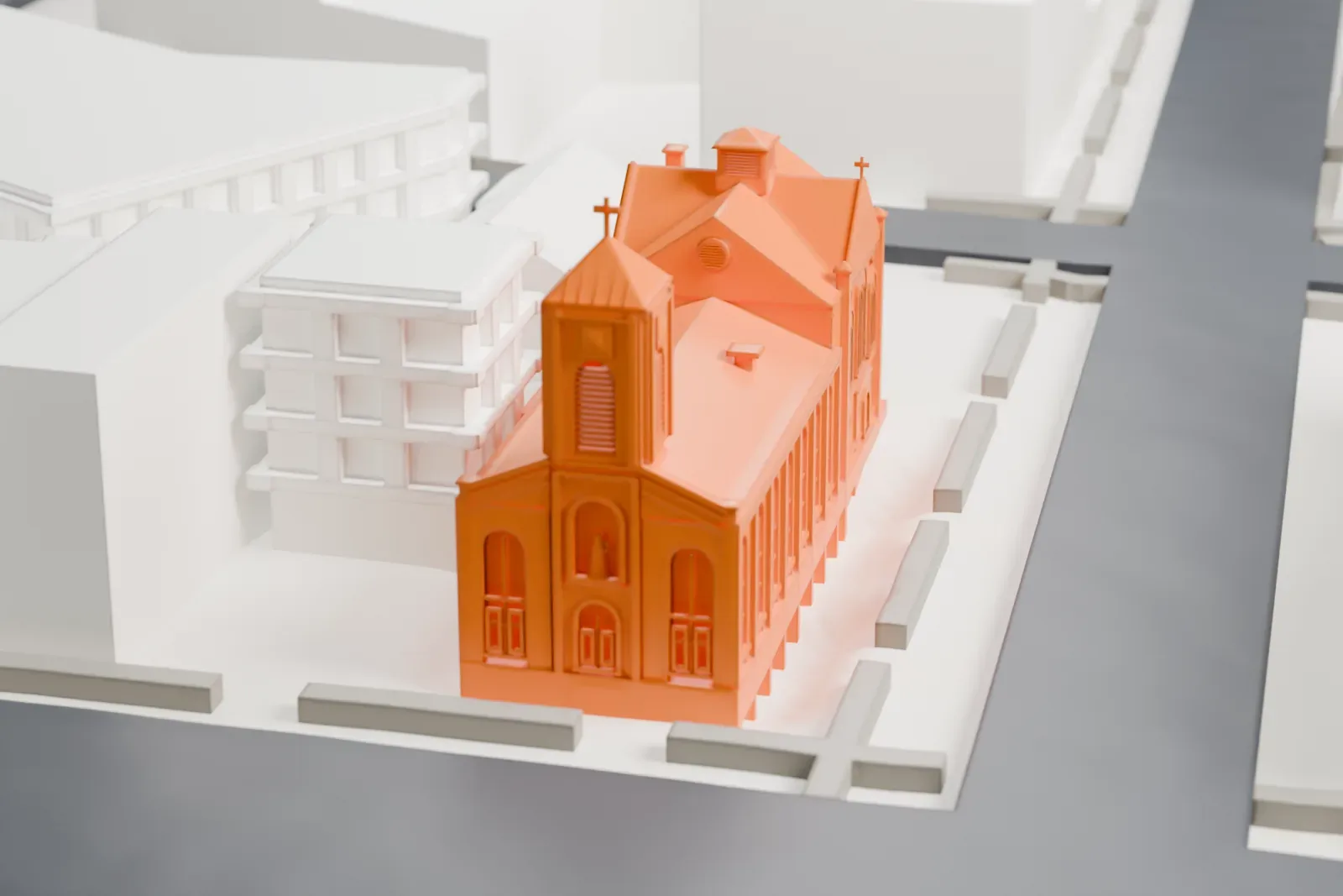 A white 3D print of St. Joseph of the Holy Family Church, a brick church with a bell tower and tall arched windows, among larger buildings.
