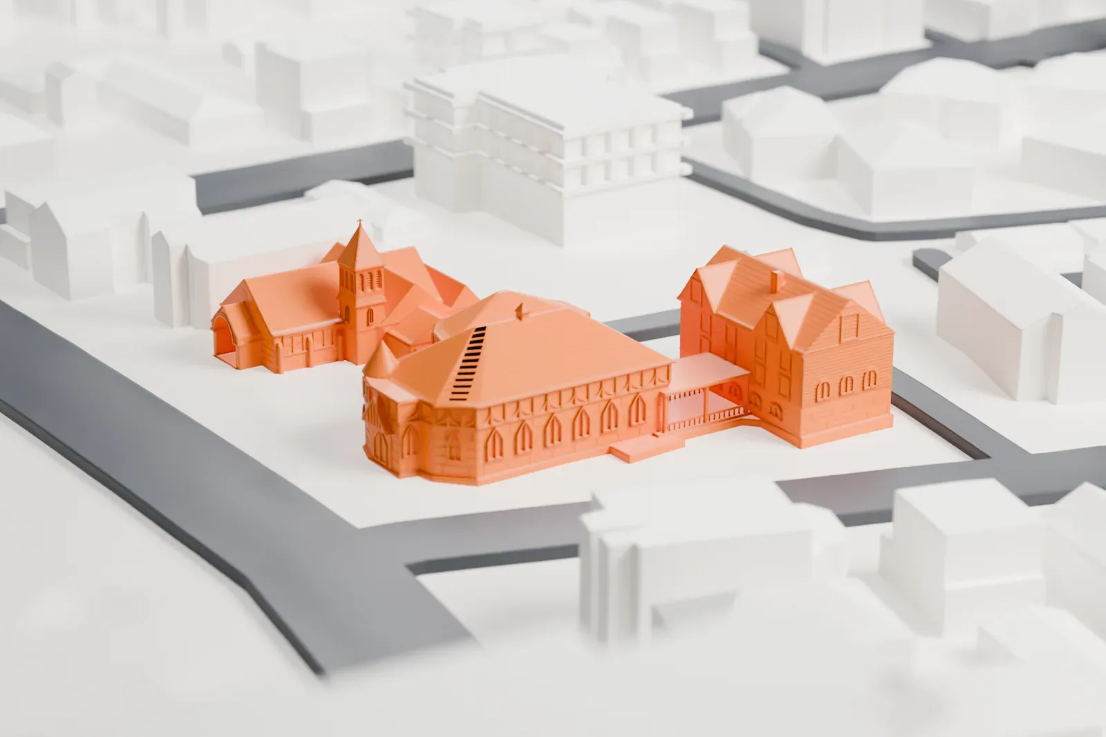 A white 3D print of St. Luke's Chapel, a group of linked buildings with gabled and hipped roofs, surrounded by streets and low buildings.
