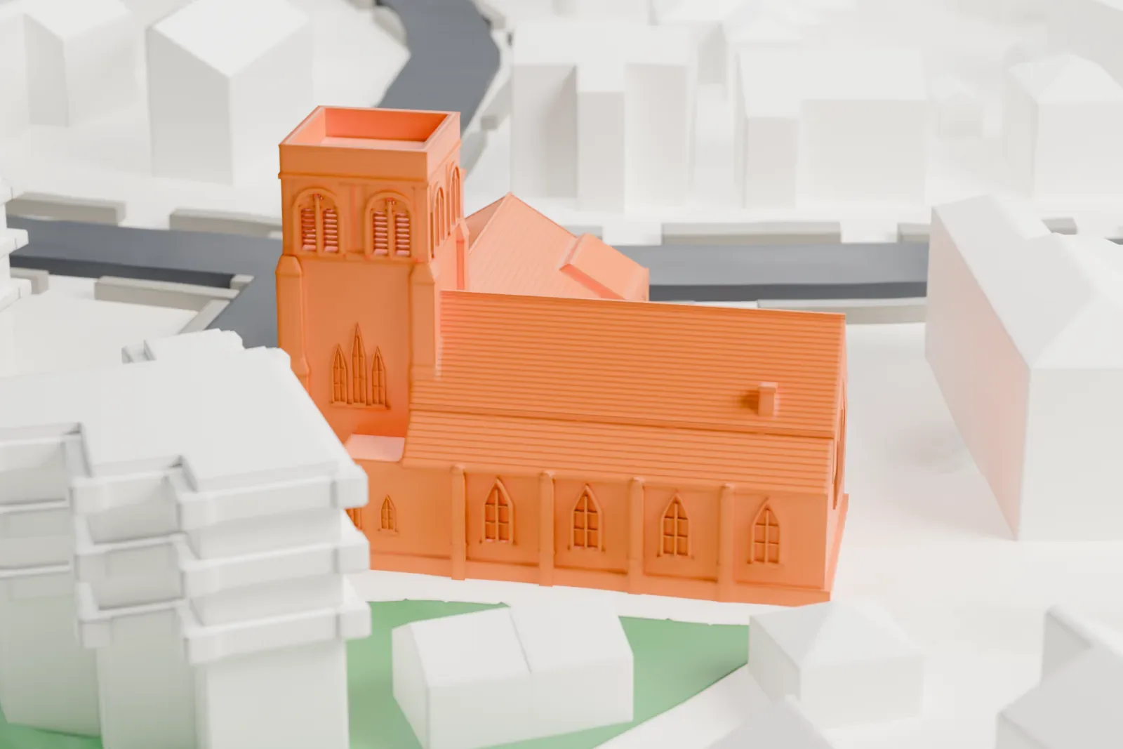 A white 3D print of St. Luke's Episcopal Church, a church with a square tower and steep roofs, on a street corner among nearby buildings and small green areas.