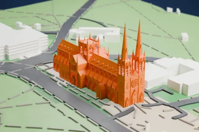A white 3D print of St Mary's Cathedral, a long Gothic church with twin spires, a central tower and a row of small gables, set in green parkland with winding paths.