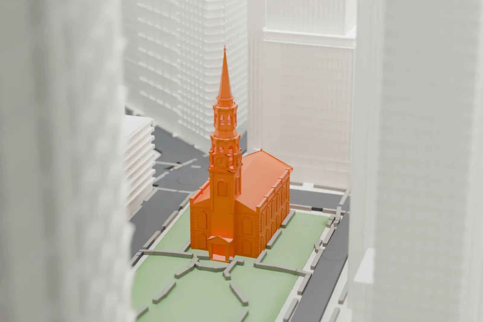 A white 3D print of St. Paul's Chapel, a small church with a slender spire beside a green churchyard, dwarfed by tall Lower Manhattan buildings.
