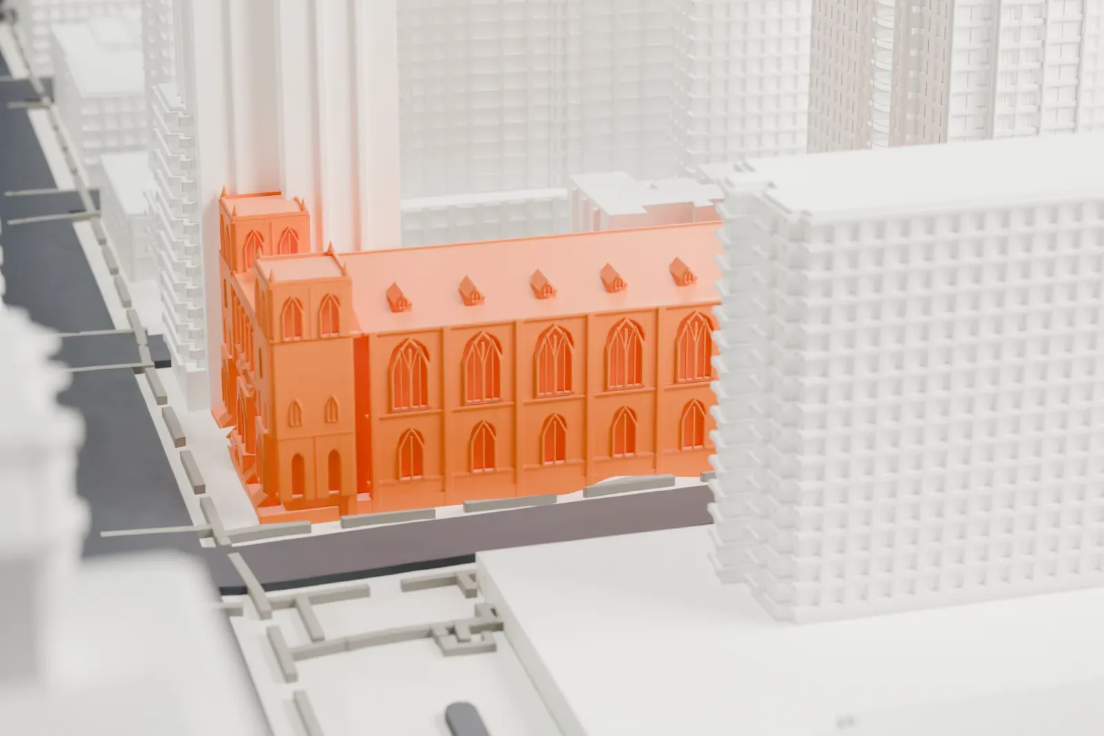 A white 3D print of the Church of St. Paul the Apostle, a small church with two towers, squeezed between much taller buildings along city streets.
