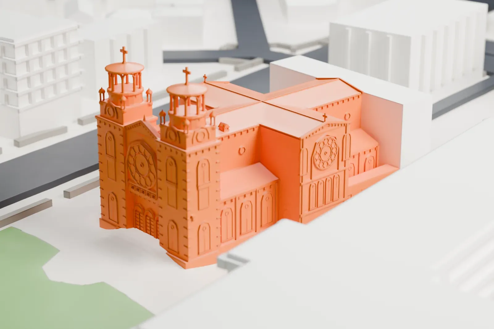 A white 3D print of St. Raymond's Church in the Bronx, a wide church with two domed towers on its front, beside a small green lawn and larger buildings.