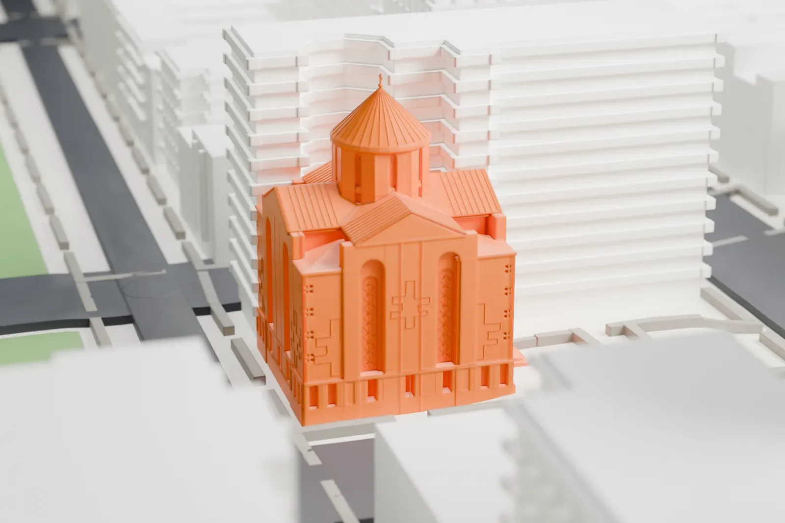 A white 3D print of St. Vartan Armenian Cathedral, a church with a pointed dome, beside a street and a small plaza with taller buildings around it.