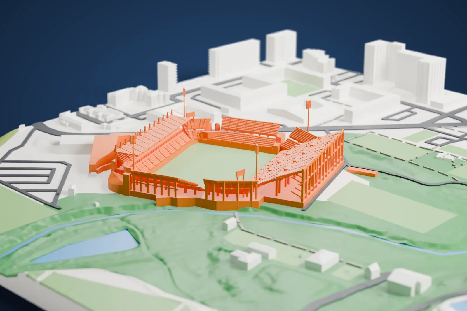 A white 3D print of Stade de la Mosson, an open football stadium with a green pitch and floodlight masts, with parkland, a stream and streets around it.