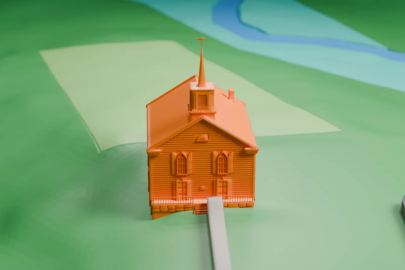 A white 3D print of Stockholm United Methodist Church, a small church with a steeple, on a green hillside beside a road with a few scattered buildings.