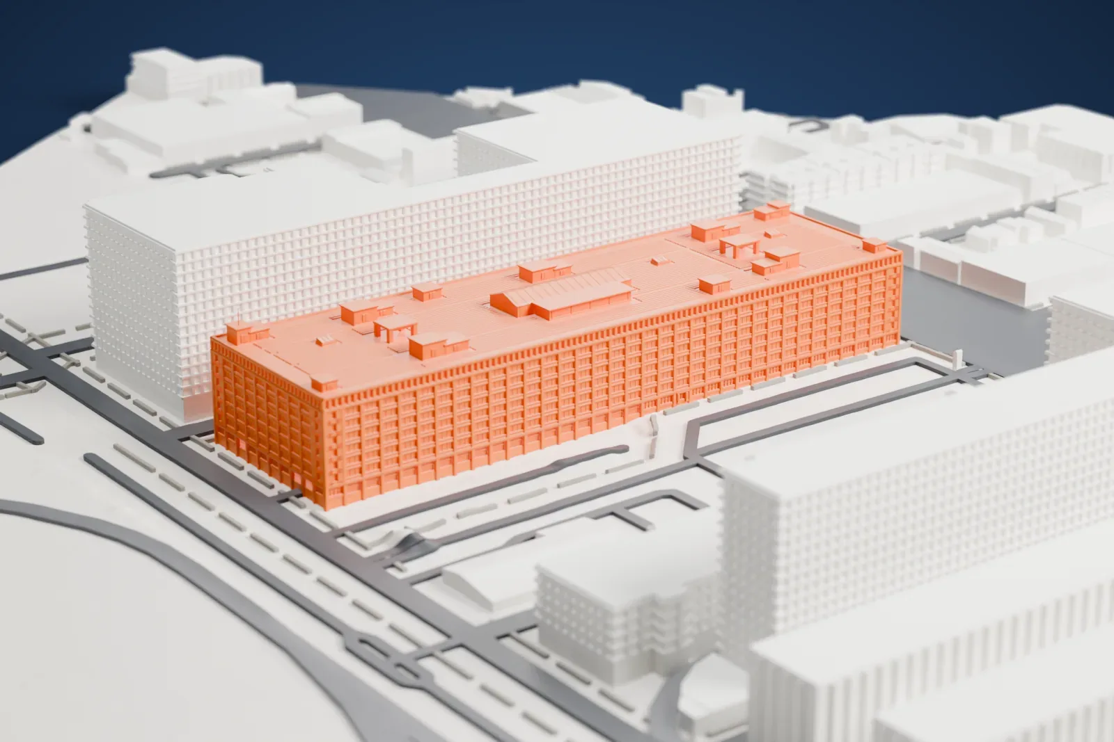 A white 3D print of a long multi-story warehouse filling a city block, beside large buildings and streets.