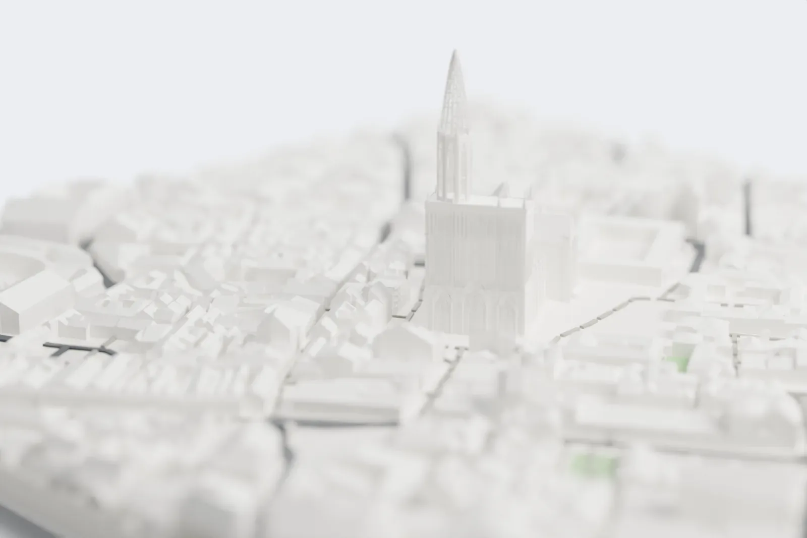 A white 3D print of Strasbourg Cathedral, a pitched-roof church with a tall tower topped by an open lattice spire, standing among dense buildings with a river nearby.