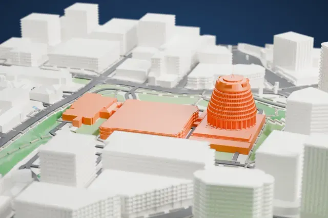 A white 3D print of the Beehive, a round stepped tower with a mast on top, standing on a square base among roads, green lawns and taller buildings.