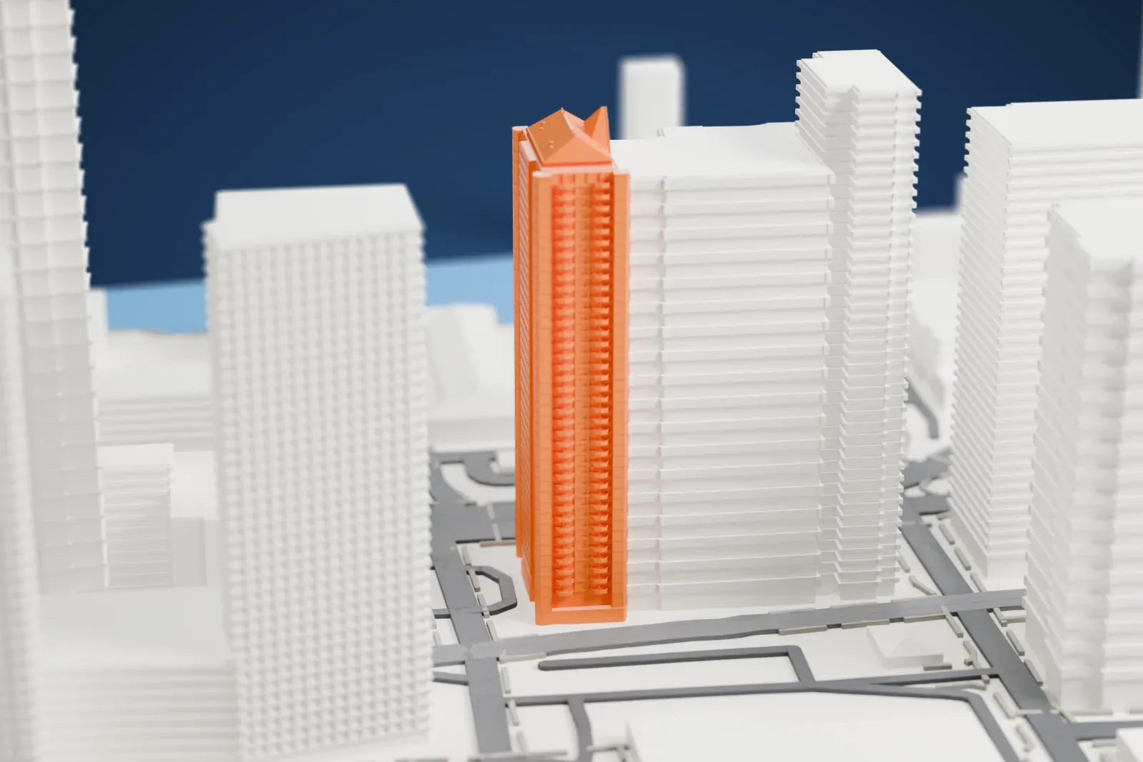 A white 3D print of one of The BLVD Collection towers, a slender tower with a pitched, gabled roof, standing among taller neighboring buildings beside a network of roads.