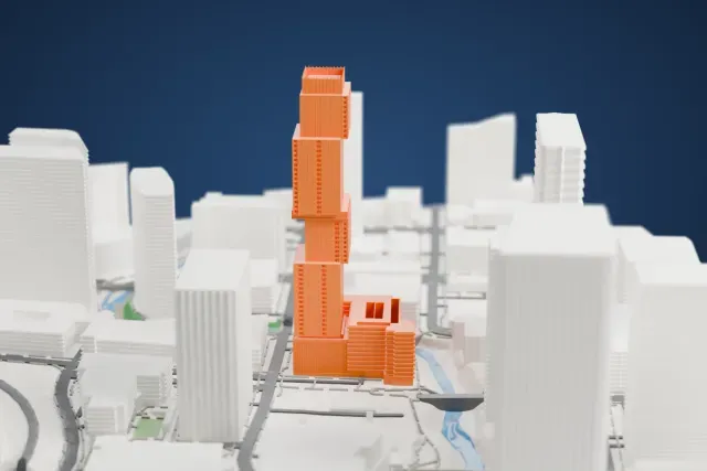 A white 3D print of The Independent, a tall tower made of offset stacked blocks with a boxy crown, rising among other high-rise buildings.