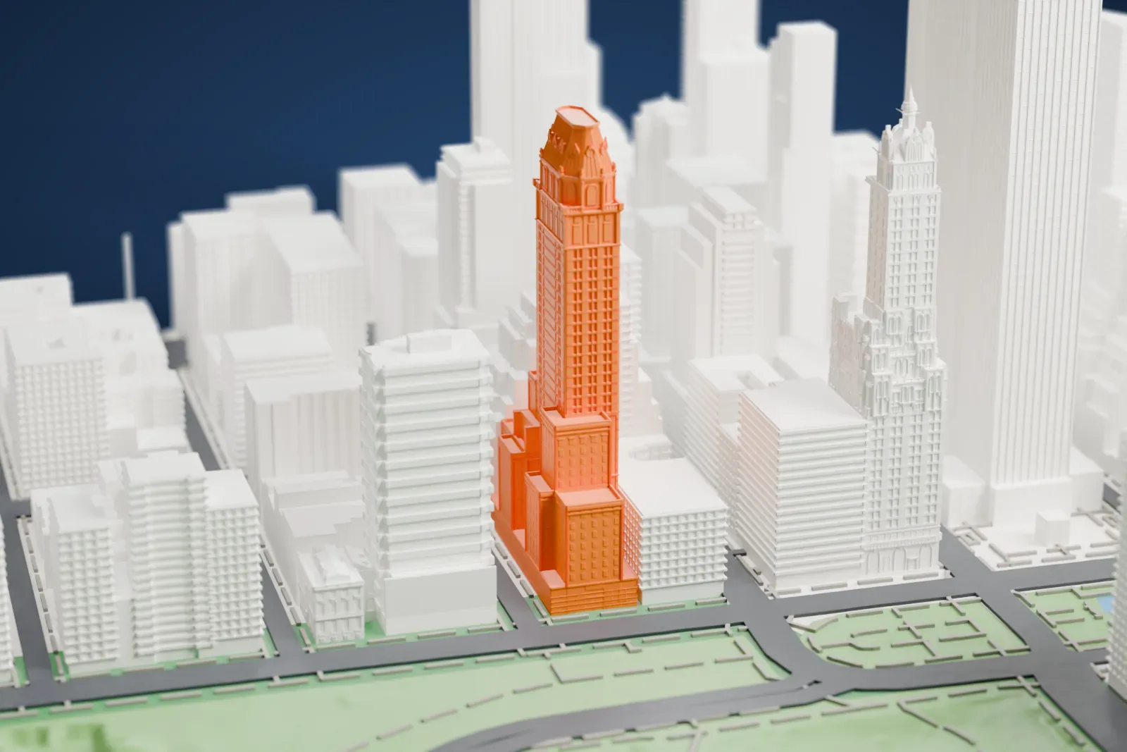 A white 3D print of The Pierre, a tall shaft with a stepped base and an ornate sloped crown, beside a park with water and surrounded by other buildings.