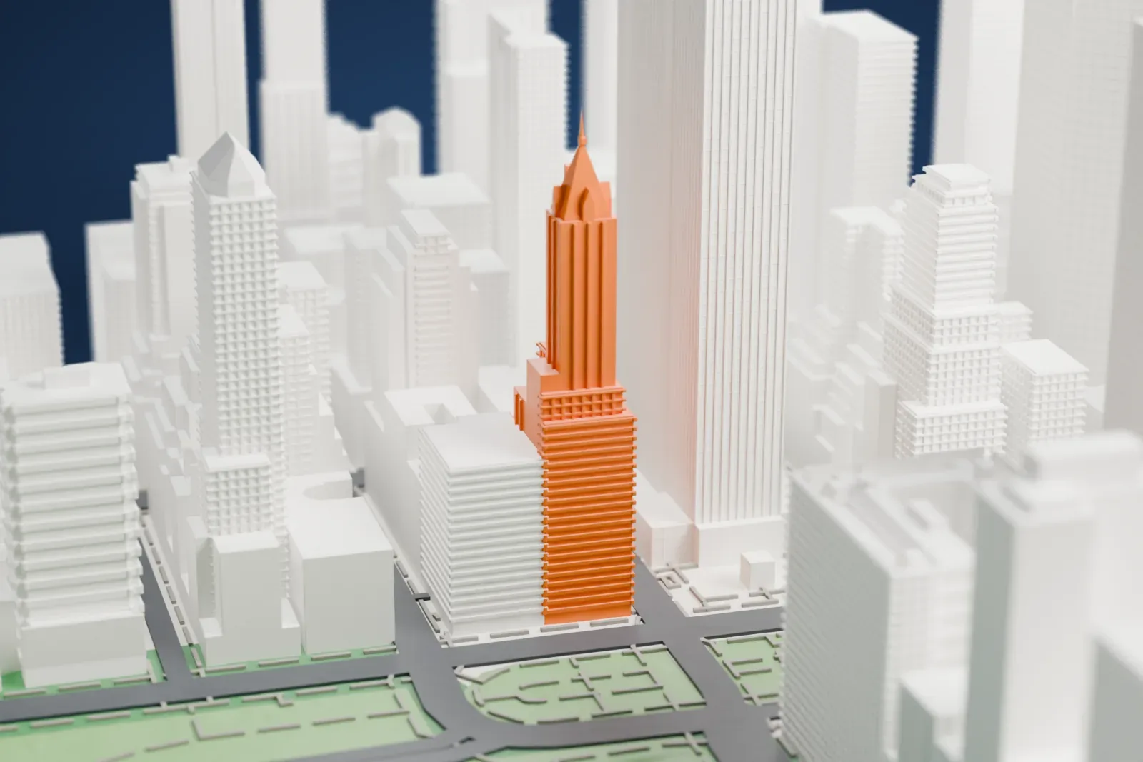A white 3D print of the Sherry-Netherland, a slender tower with an ornate pinnacled crown and thin spire, rising among Upper East Side buildings beside a green park with a pond.
