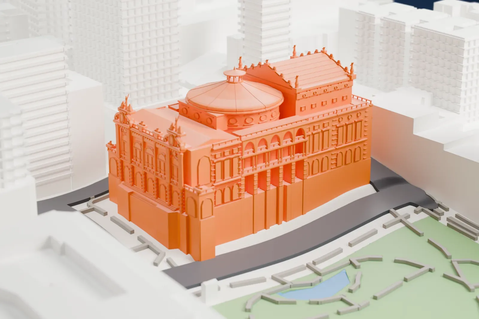 A white 3D print of the Theatro Municipal (São Paulo), with a rounded roof and small rooftop figures, surrounded by streets, tall buildings, and park areas.