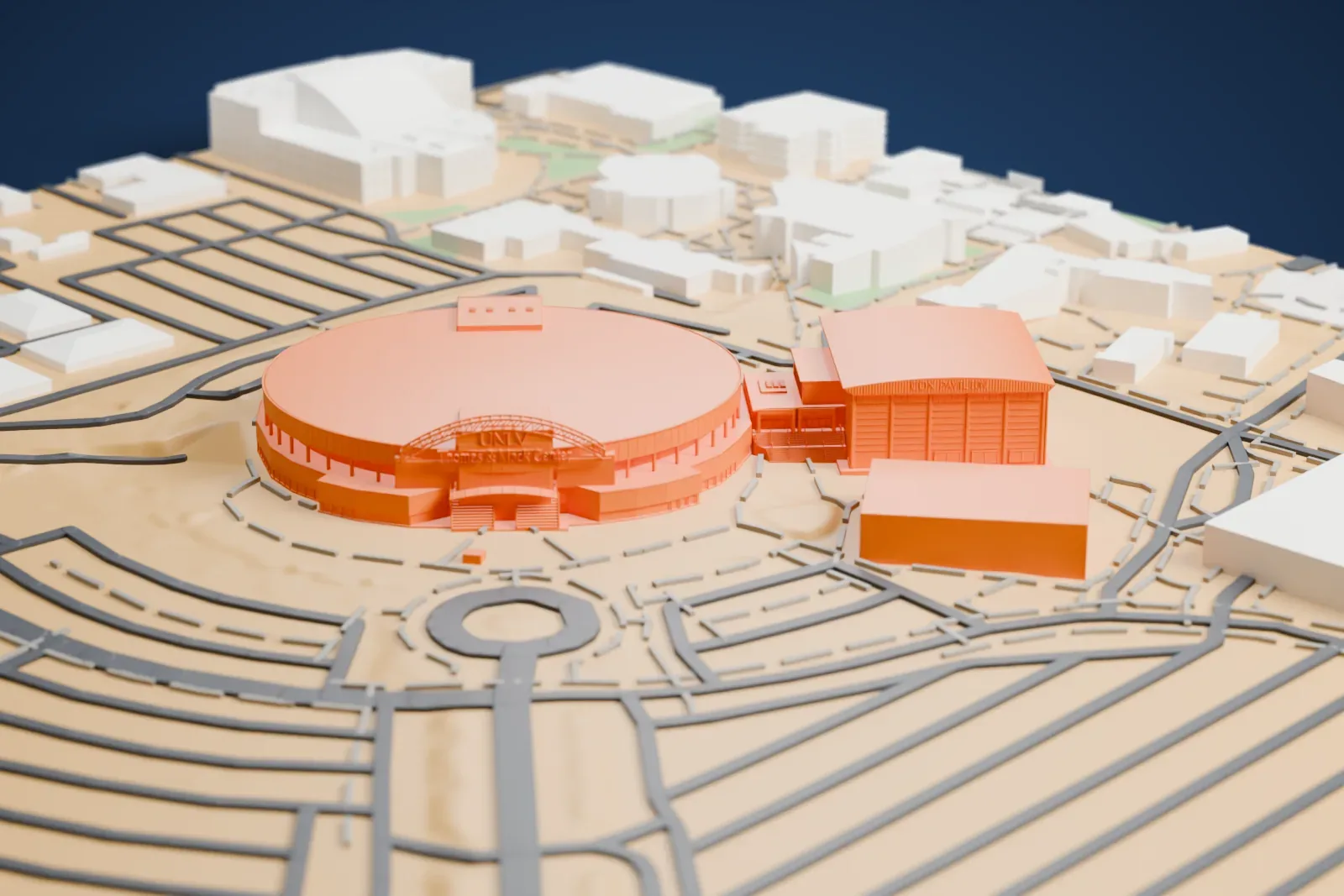 A white 3D print of the Thomas & Mack Center, a wide round arena with a low roof and an arched entrance, beside a hall with an arched roof and ringed by roads.
