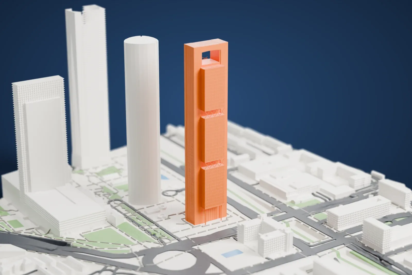 A white 3D print of Torre Cepsa, a tall slim tower of stacked blocks with X-shaped braces and an open frame at the top, among neighboring towers, roads and green patches.