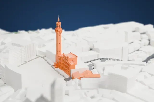 A white 3D print of the Torre del Mangia, a tall slender tower with a crenellated top and a thin spire, beside a battlemented palace and a curved open square ringed by dense buildings.