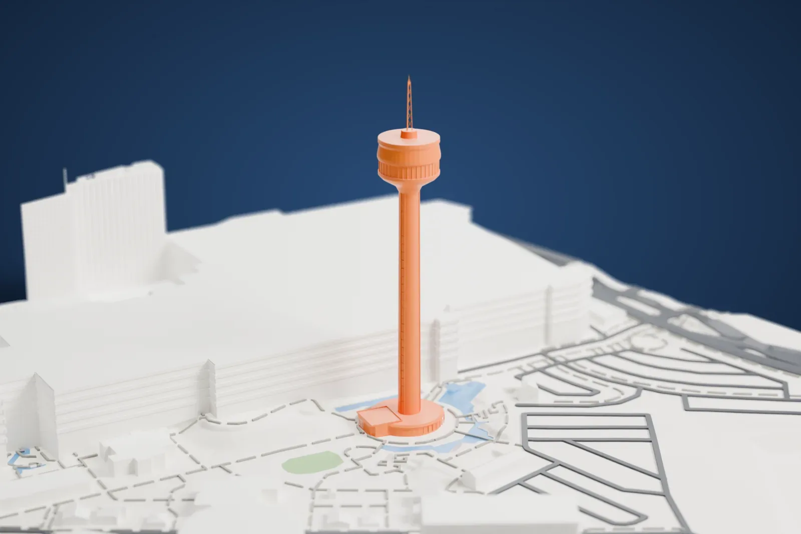 A white 3D print of the Tower of the Americas, a slim shaft with a saucer-shaped top house and a thin antenna, standing beside large buildings, roads and pools of water.