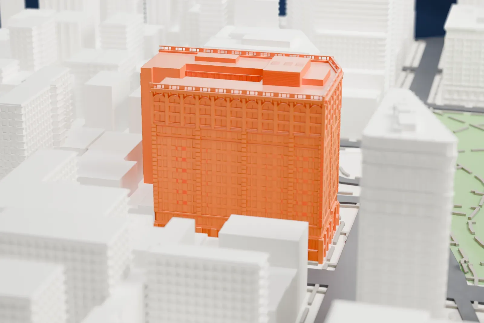 A white 3D print of the Toy Center, a large corner building beside a green square, with a second slimmer tower farther off among dense city blocks.