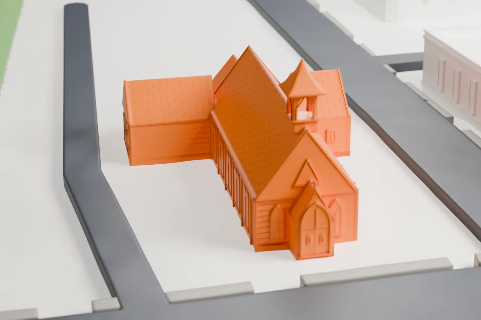 A white 3D print of Trinity Chapel, a long gabled chapel with a small belfry and low side wings, on a block bordered by roads with larger buildings nearby.