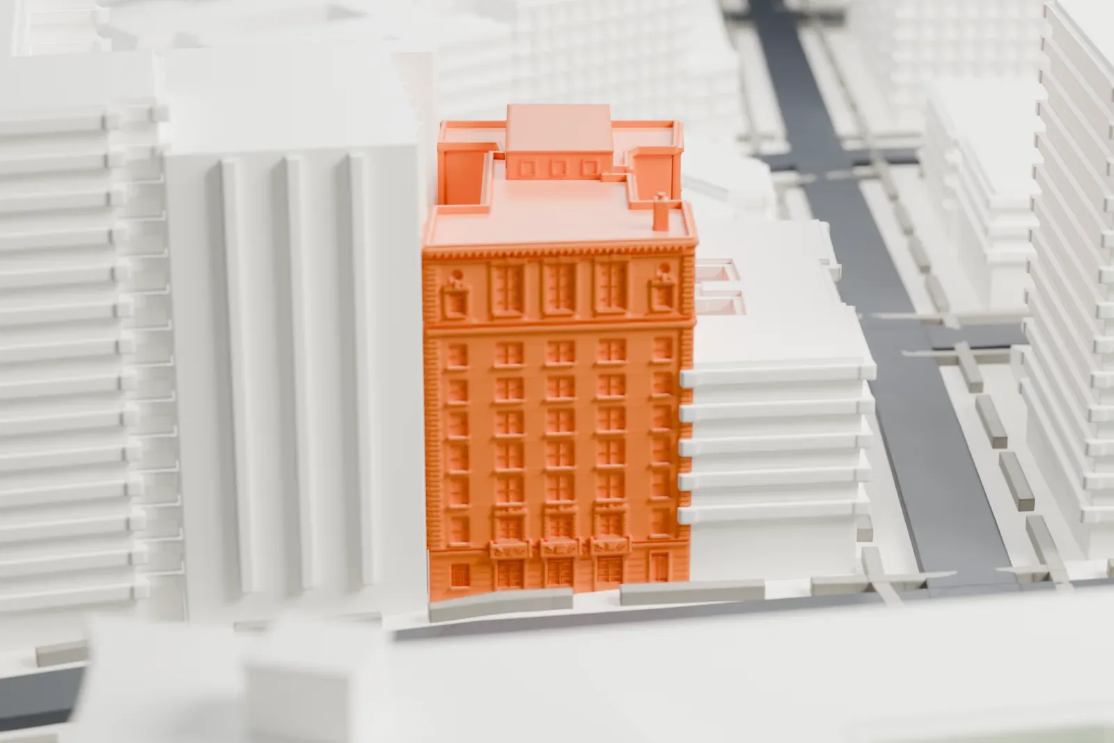 A white 3D print of the Union Temple of Brooklyn's tall building, with stepped upper floors, among neighboring buildings beside a patch of green.