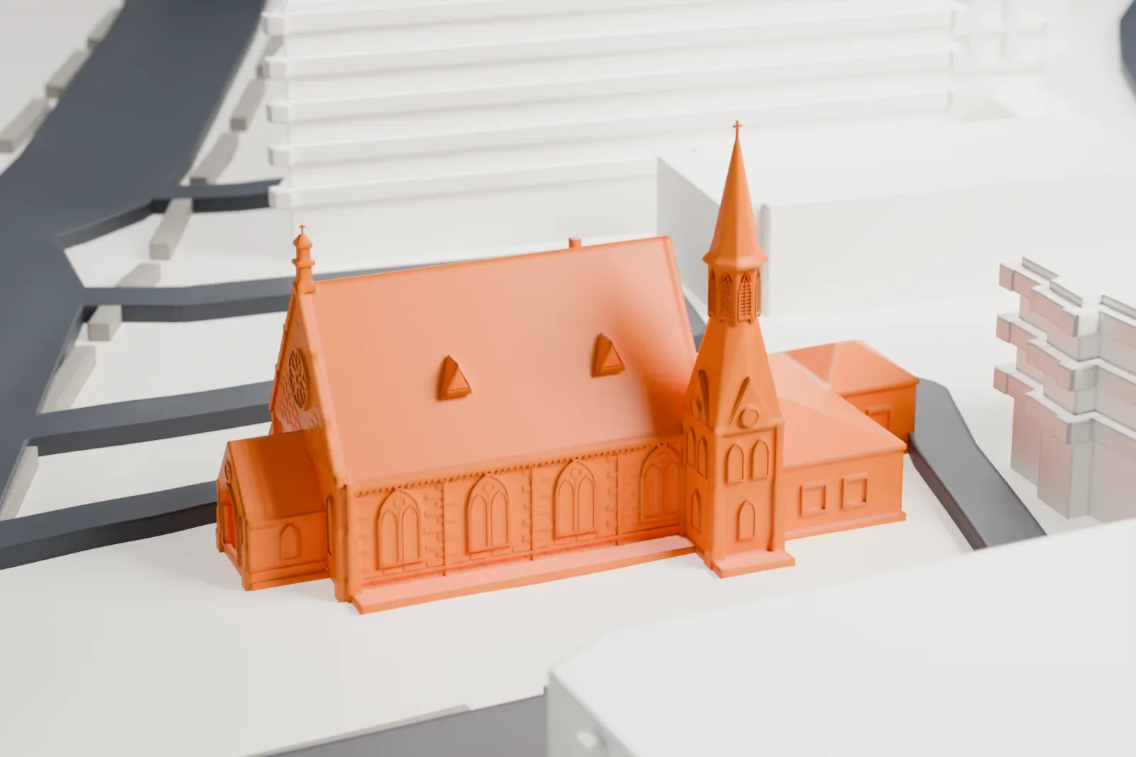 A white 3D print of a Gothic Revival church with a pointed spire, surrounded by taller buildings and streets.