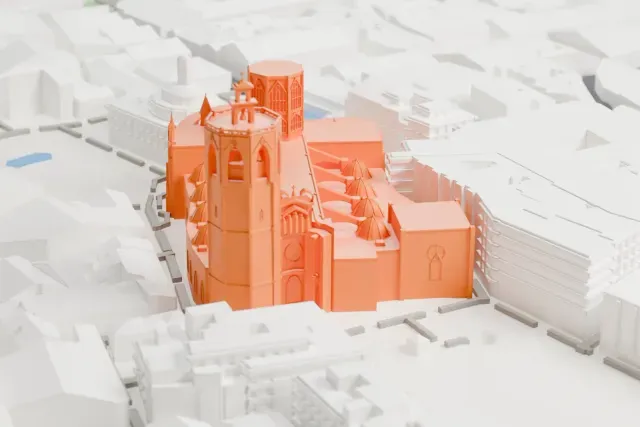 A white 3D print of Valencia Cathedral, a long church with a tall octagonal tower and a row of small domes, surrounded by dense blocks of buildings and narrow streets.