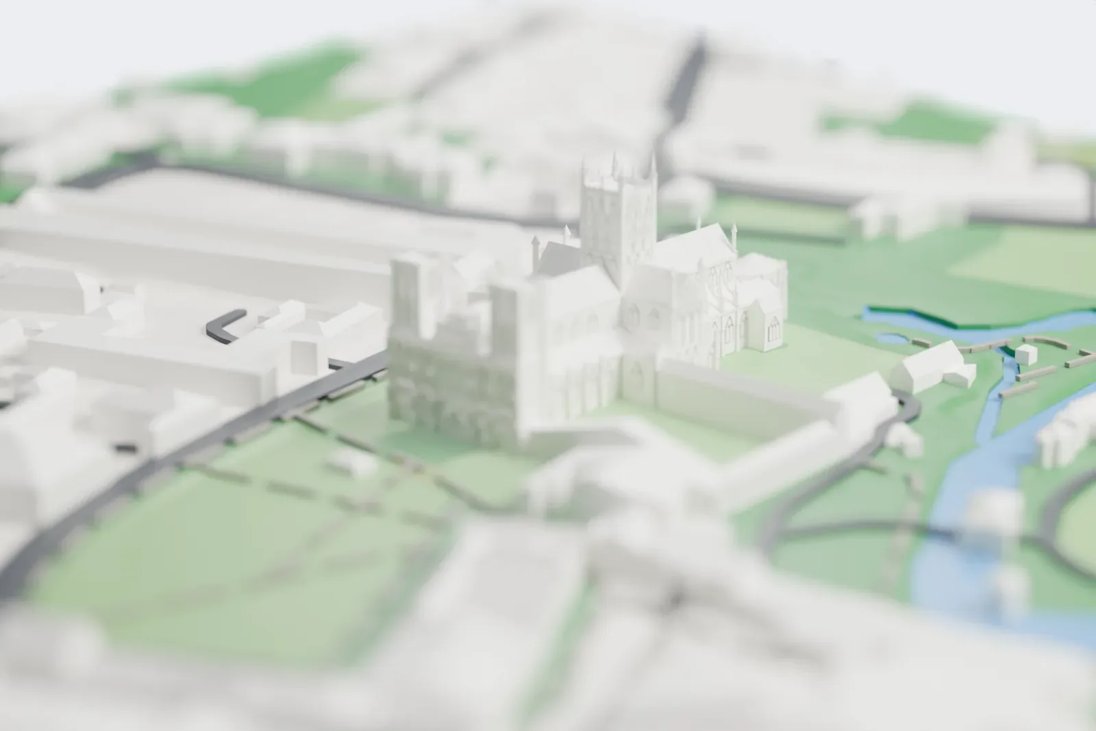 A white 3D print of Wells Cathedral, a cruciform church whose tall central tower has slender corner pinnacles, with two west towers and an eight-sided chapel at the east end, among lawns and a river.