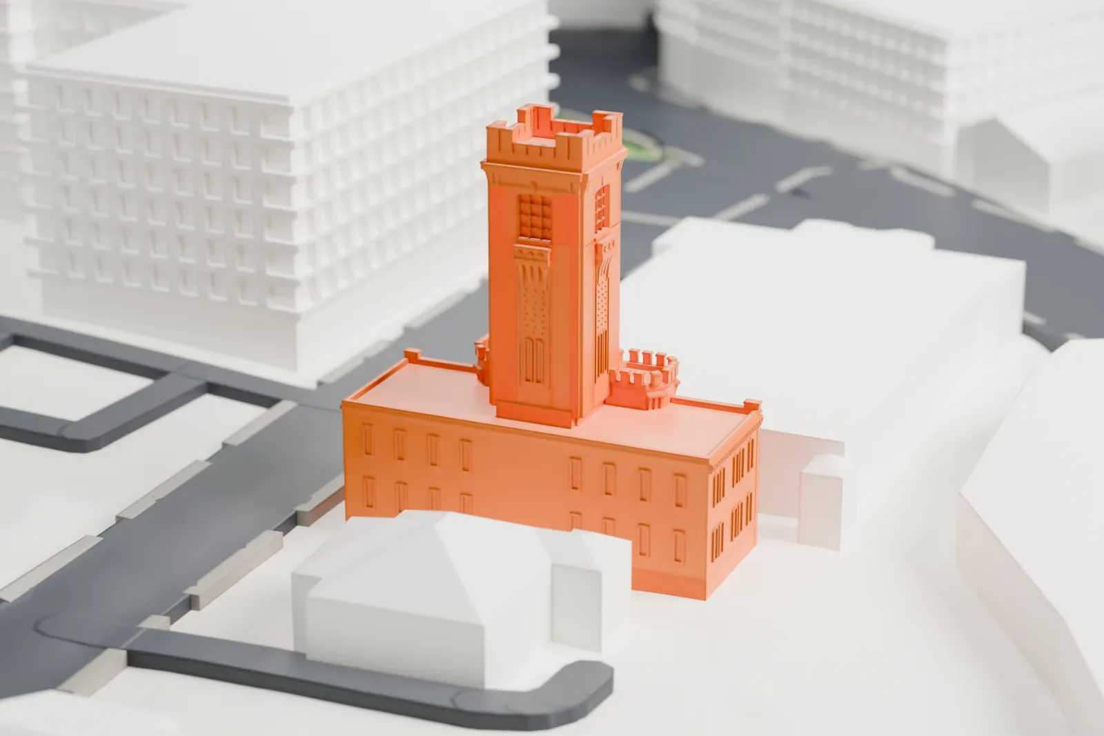 A white 3D print of the White Plains Armory, a building with a tall battlemented tower, surrounded by streets and larger neighboring buildings.