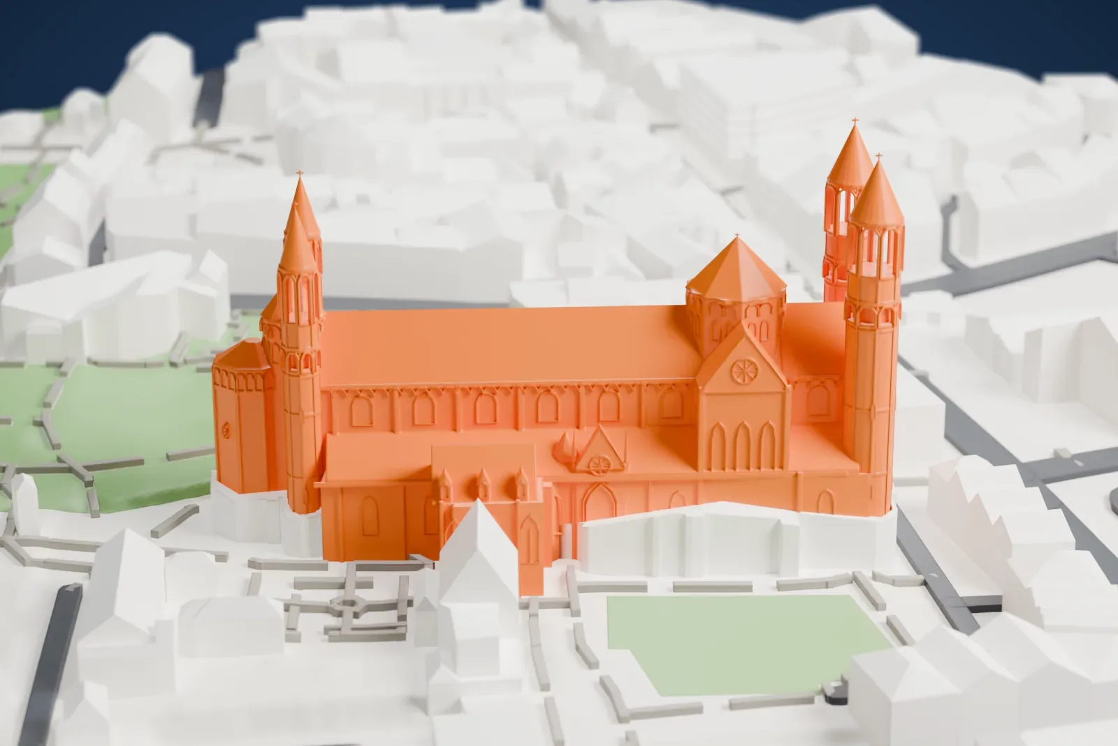 A white 3D print of the Worms Cathedral with pointed tower roofs and a long nave, surrounded by buildings, streets, paths, and green spaces.
