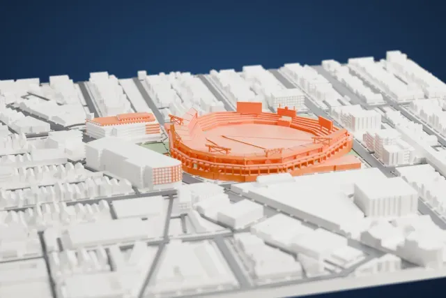 A white 3D print of Wrigley Field, an open baseball park with tiered stands curving around a field and a scoreboard in the outfield, packed in among dense city blocks.