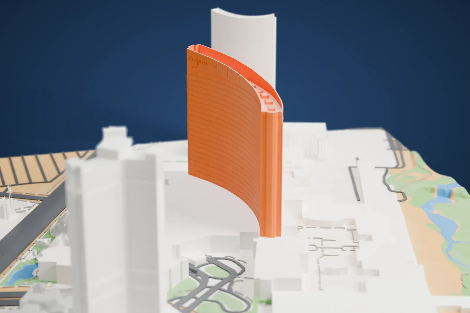 A white 3D print of Wynn Las Vegas, a tall curved tower with horizontal bands and a script logo near the top, standing among low buildings and roads.