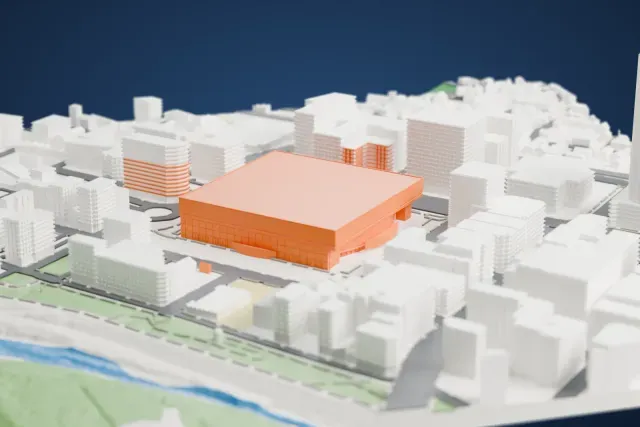 A white 3D print of Yokohama Arena, a large square block with a broad flat roof, surrounded by closely packed buildings and streets.