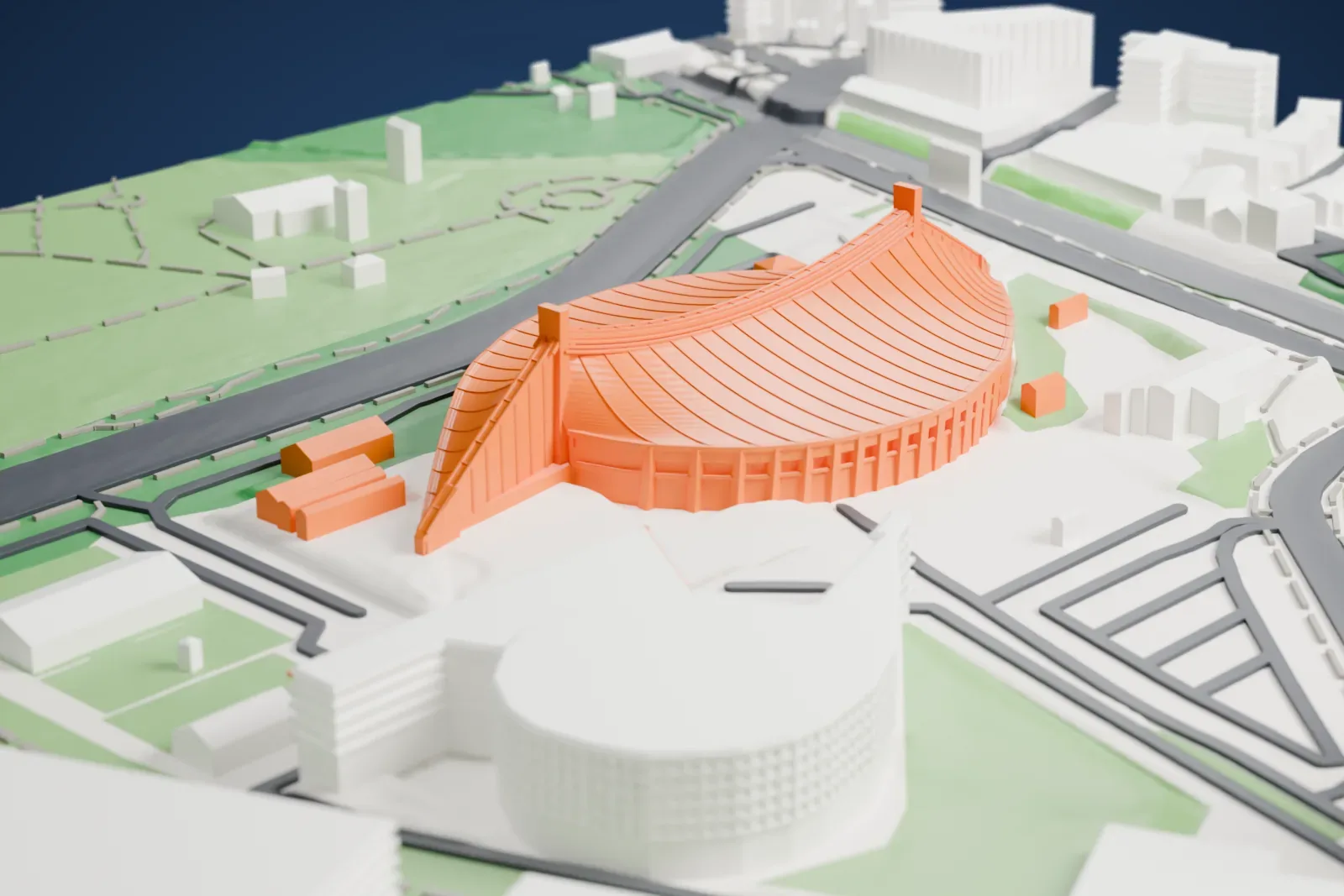 A white 3D print of Yoyogi National Gymnasium, an arena with a sweeping ribbed roof that tapers to pointed ends, set in a park with roads and low buildings around it.