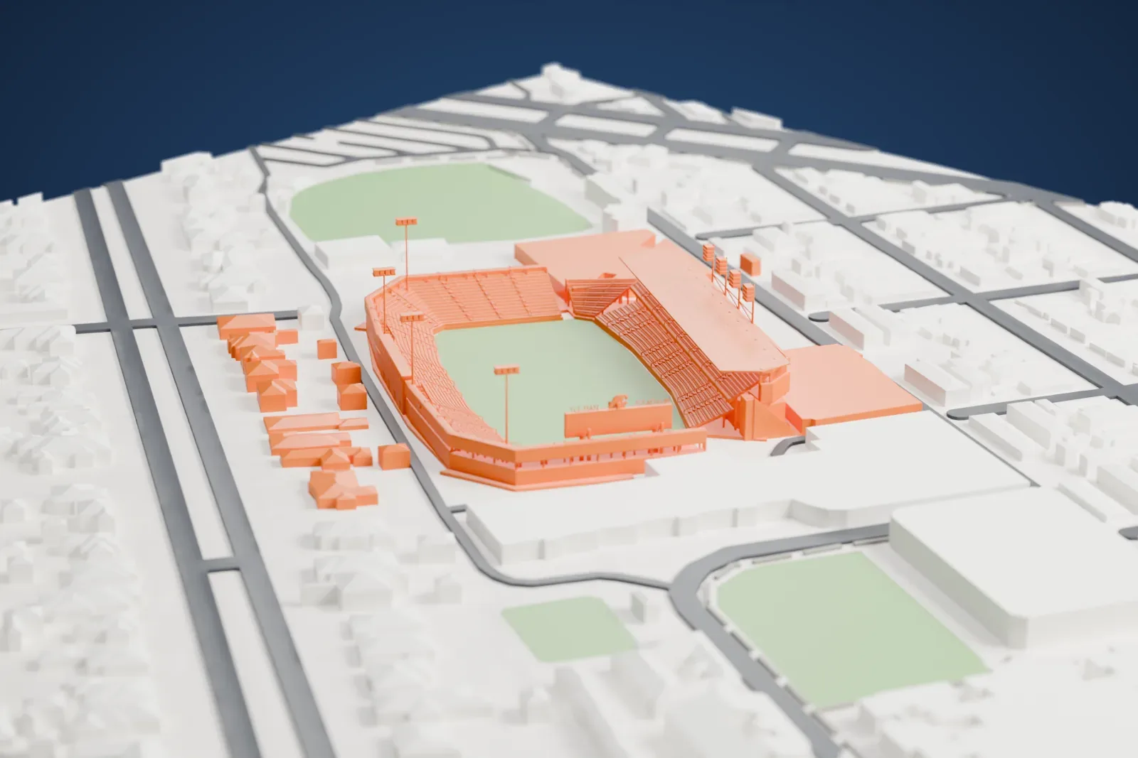 A white 3D print of Yulman Stadium, an open bowl of seating around a green field with a roofed stand on one side and tall light poles, among low buildings, streets and nearby green fields.