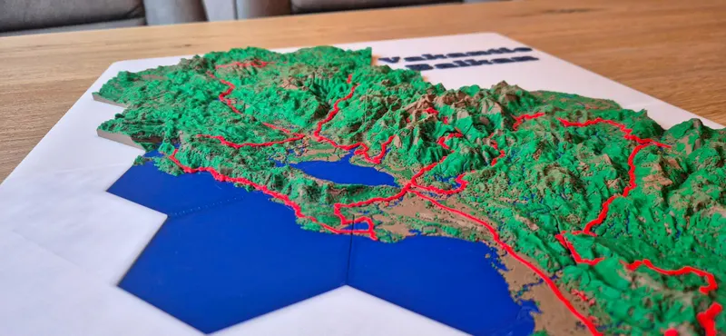 Close-up of 3D printed hexagon terrain tiles: green mountains, a red route along the coast and a blue lake and sea.