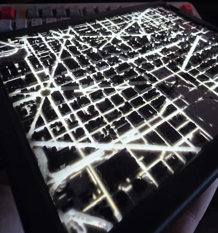 Backlit 3D printed city map with dark buildings over glowing streets.
