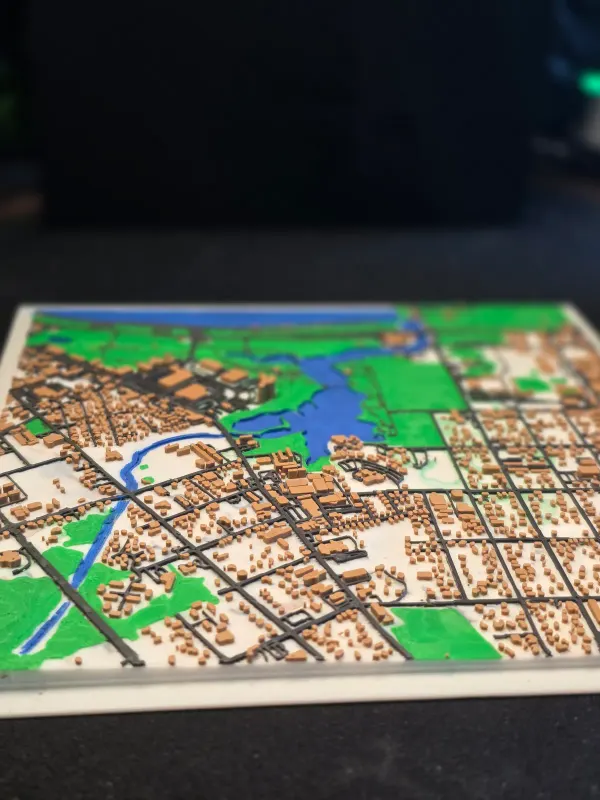 3D printed map of a city neighborhood with a river, a lake and parks.