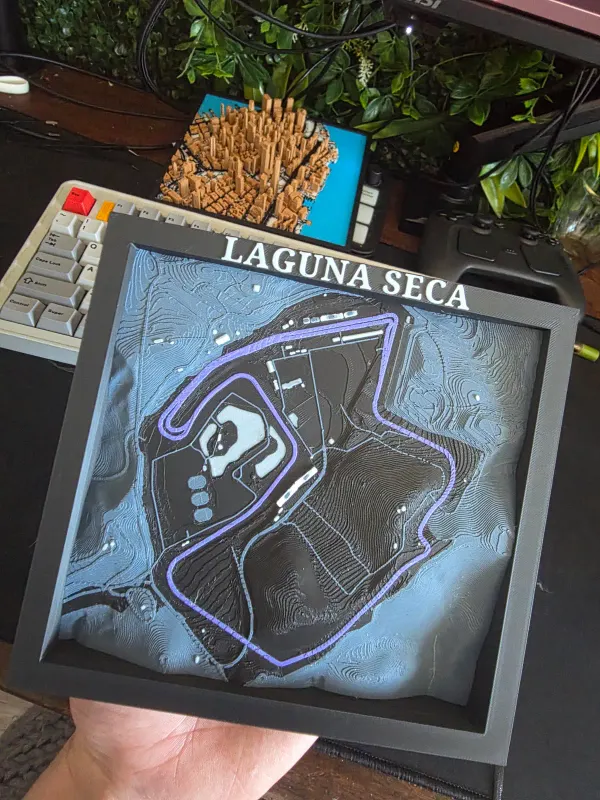 Framed 3D printed terrain map of the Laguna Seca racetrack with the lap in purple, held in a hand.