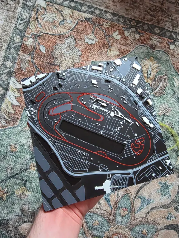 3D printed racetrack map in gray with the lap in red, held over a rug.