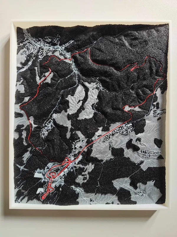 Framed 3D printed terrain map with dark forest and pale open fields over the hills and a long red route through the valleys.
