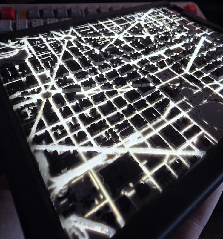 Backlit 3D printed city map with dark buildings over glowing streets.