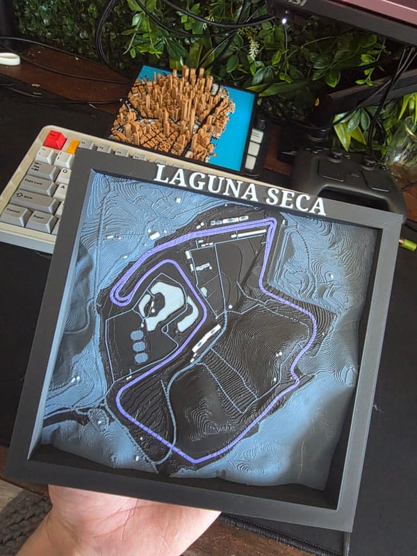 Framed 3D printed terrain map of a racetrack, with the track in purple over contour lines.